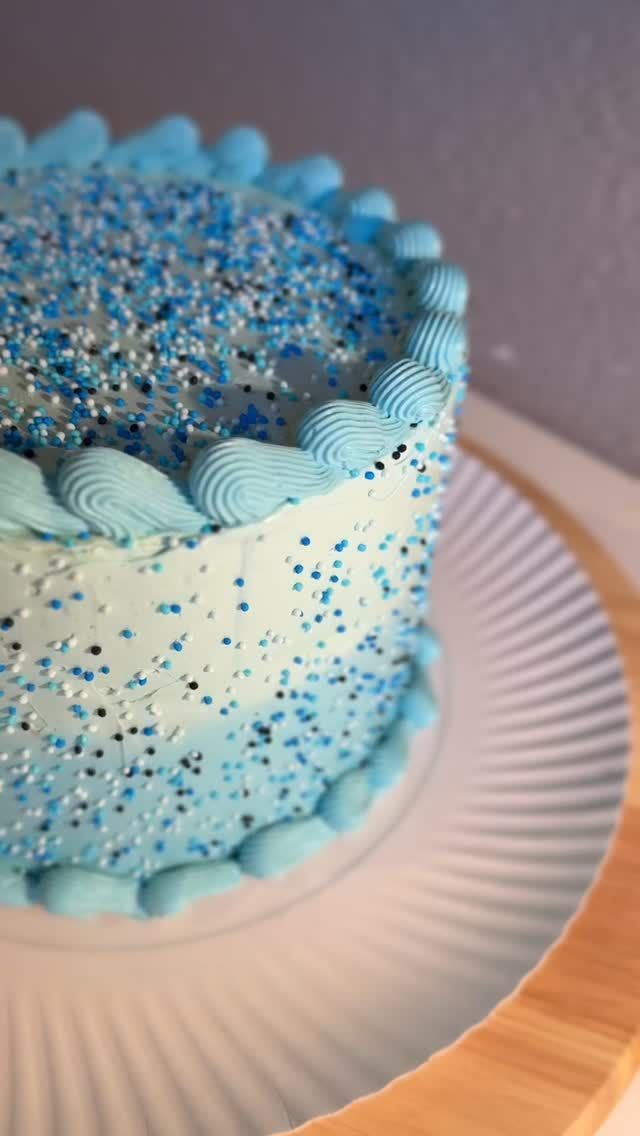 Auftragstorte mit hellblauer Creme und bunten Streuseln auf einer Tortenplatte