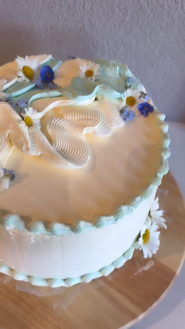 Torte mit hellblauer Buttercreme, Wellenmuster und echten Gänseblümchen