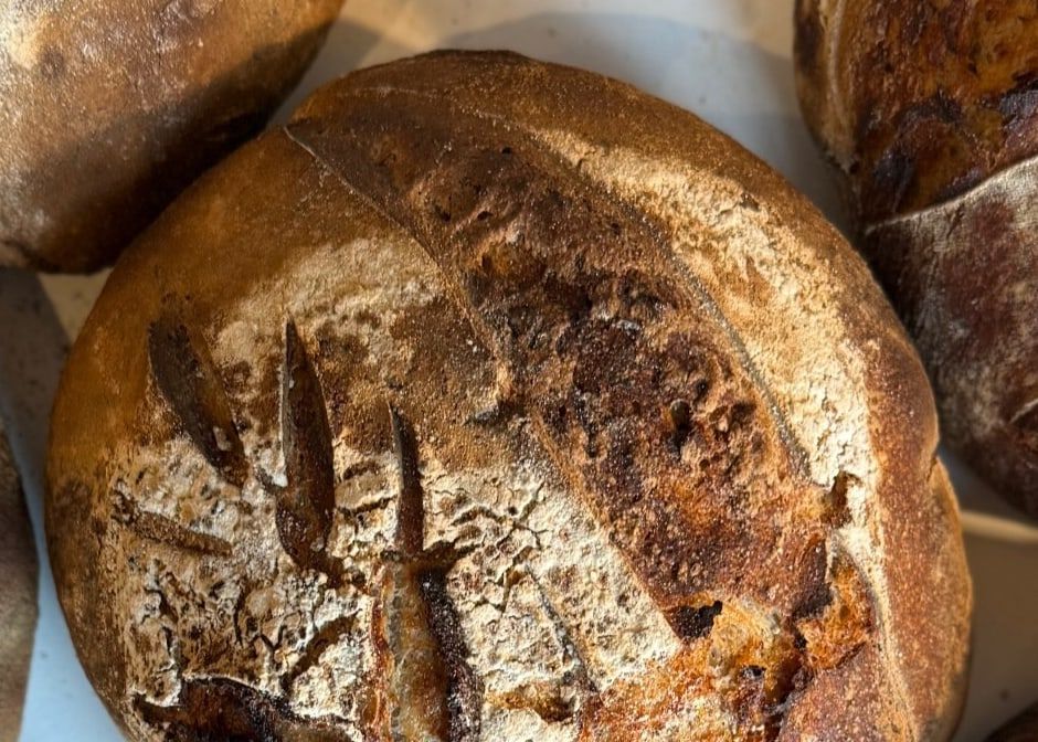 Frisch gebackene Sauerteiglaibe mit eingeschnittenem Ährenmuster und bemehlter Kruste