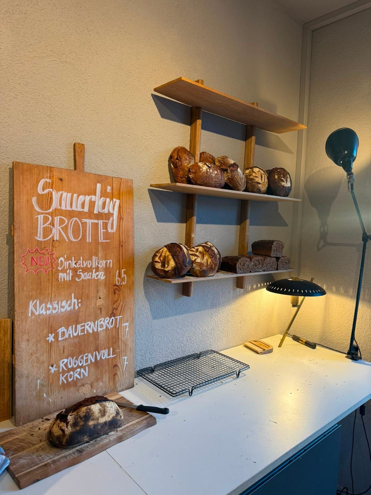 Brotregal mit Sauerteigbroten und Tafel: Dinkelvollkorn mit Saaten, Bauernbrot, Roggenvollkorn